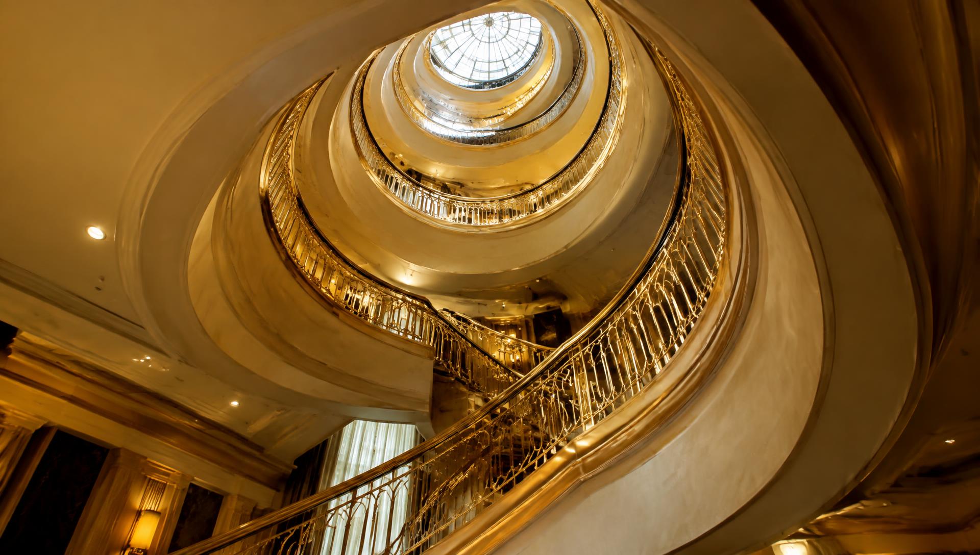 Grand spiral staircase with gold railings ascending toward a skylight